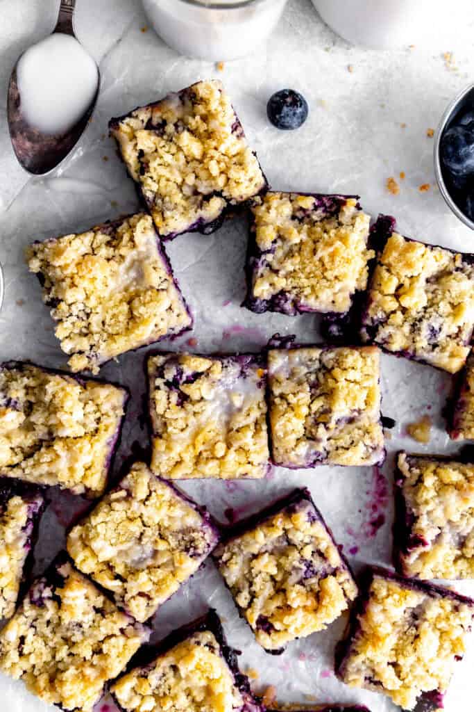 Lemon blueberry bars on a white surface, a cup of blueberries and a jug of milk.