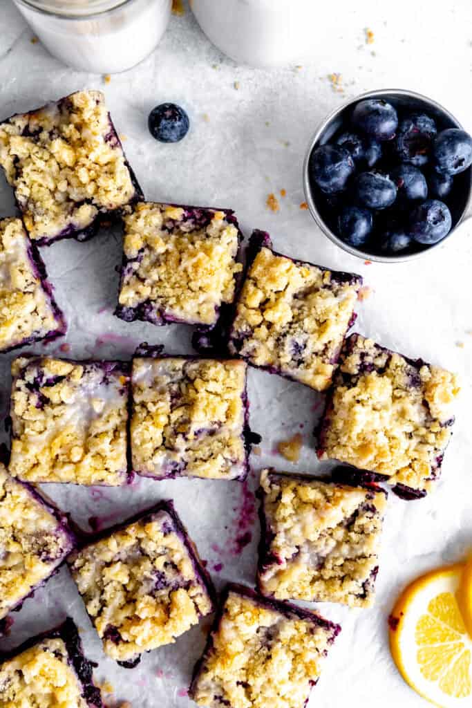 Lemon blueberry bars on a white surface, a cup of blueberries and a jug of milk.