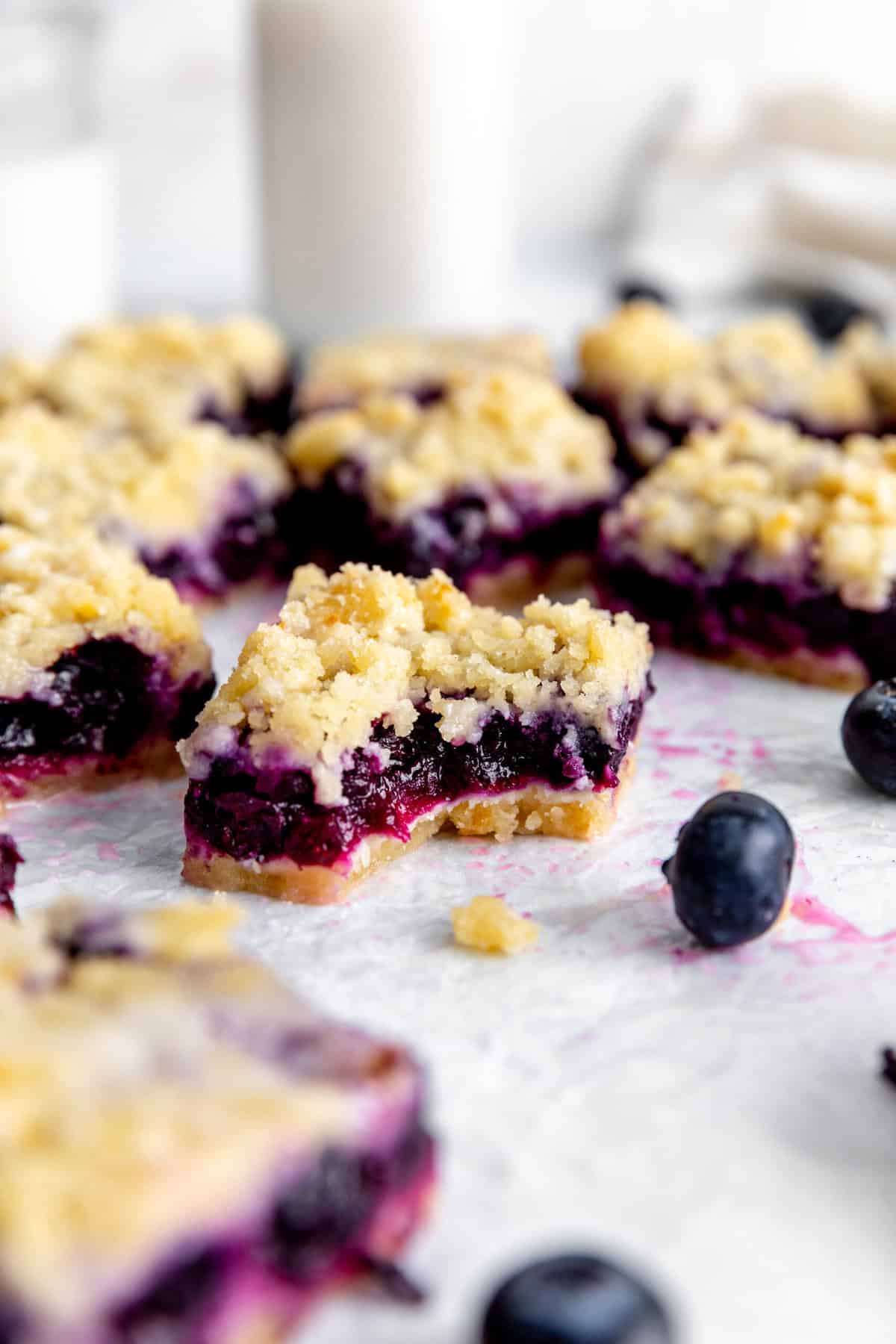 Lemon blueberry bar with a bite taken out of it surrounded by fresh blueberries.