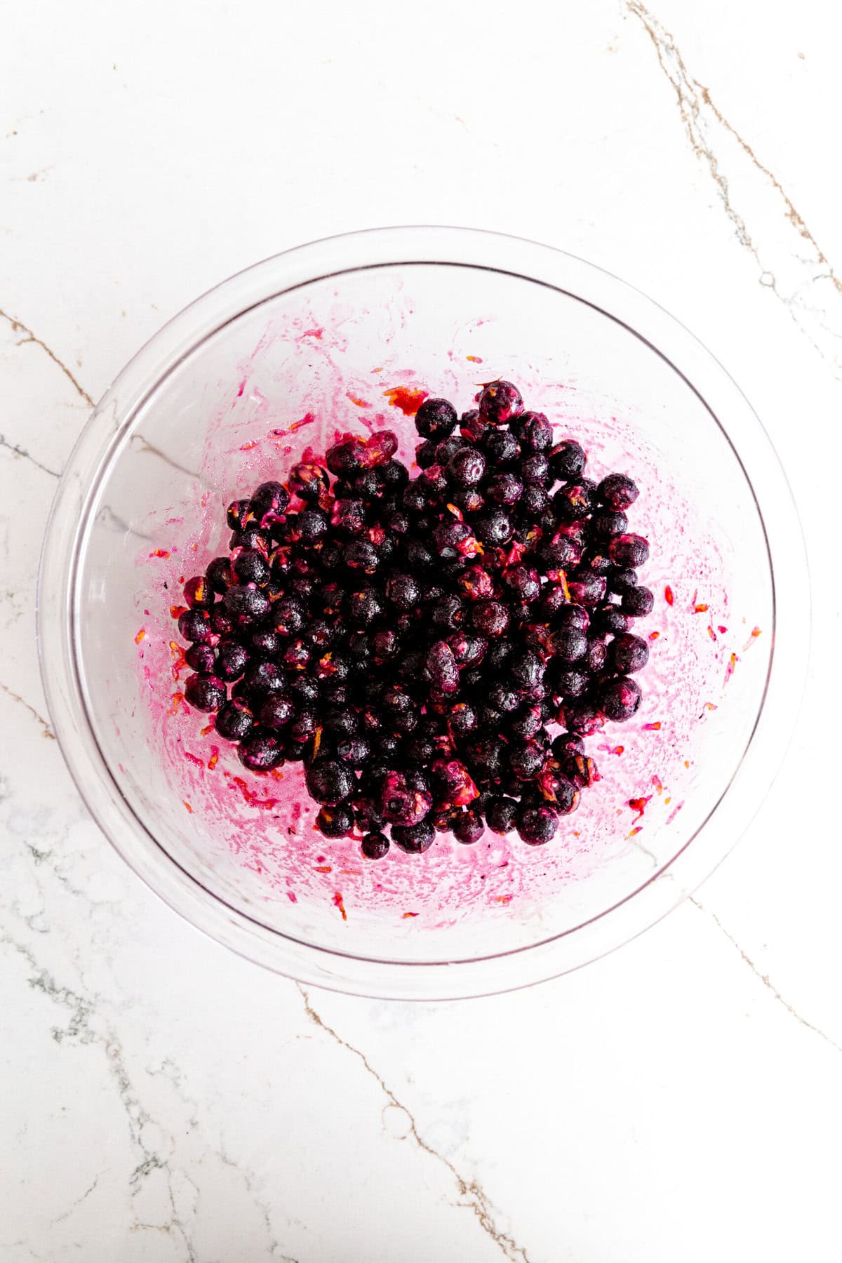 Glass bowl filled with frozen blueberries tossed in sugar.