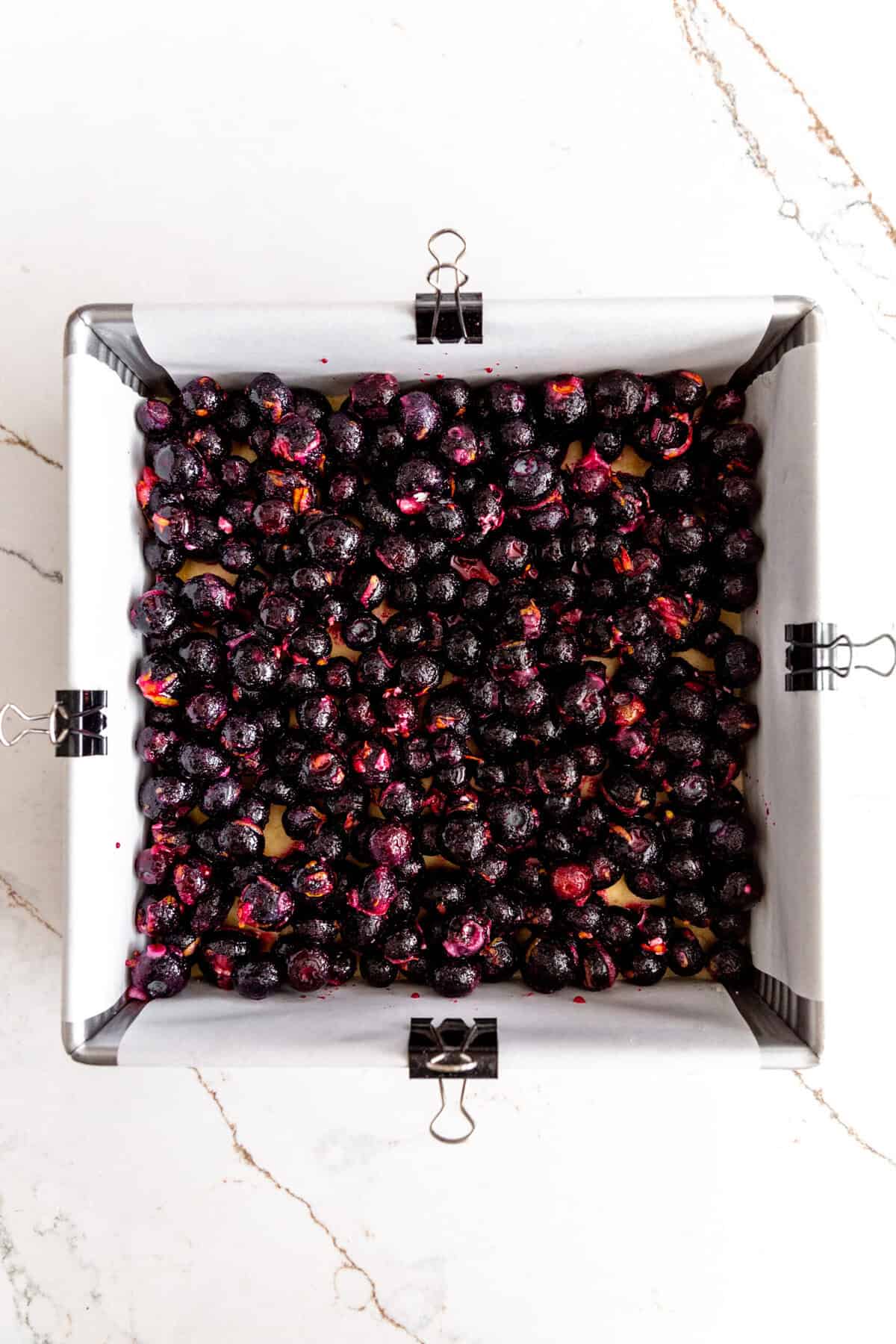 Frozen blueberries spread over unbaked crust in a square baking pan.