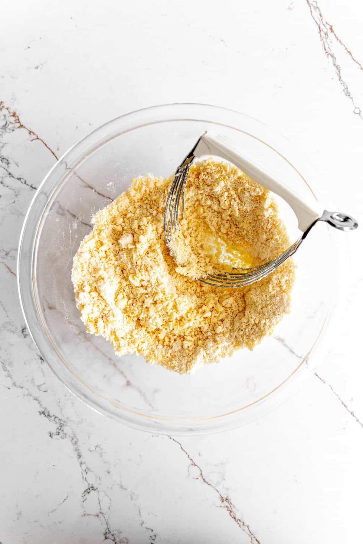 Glass bowl filled with crumbly butter, sugar and flour and a pastry cutter.