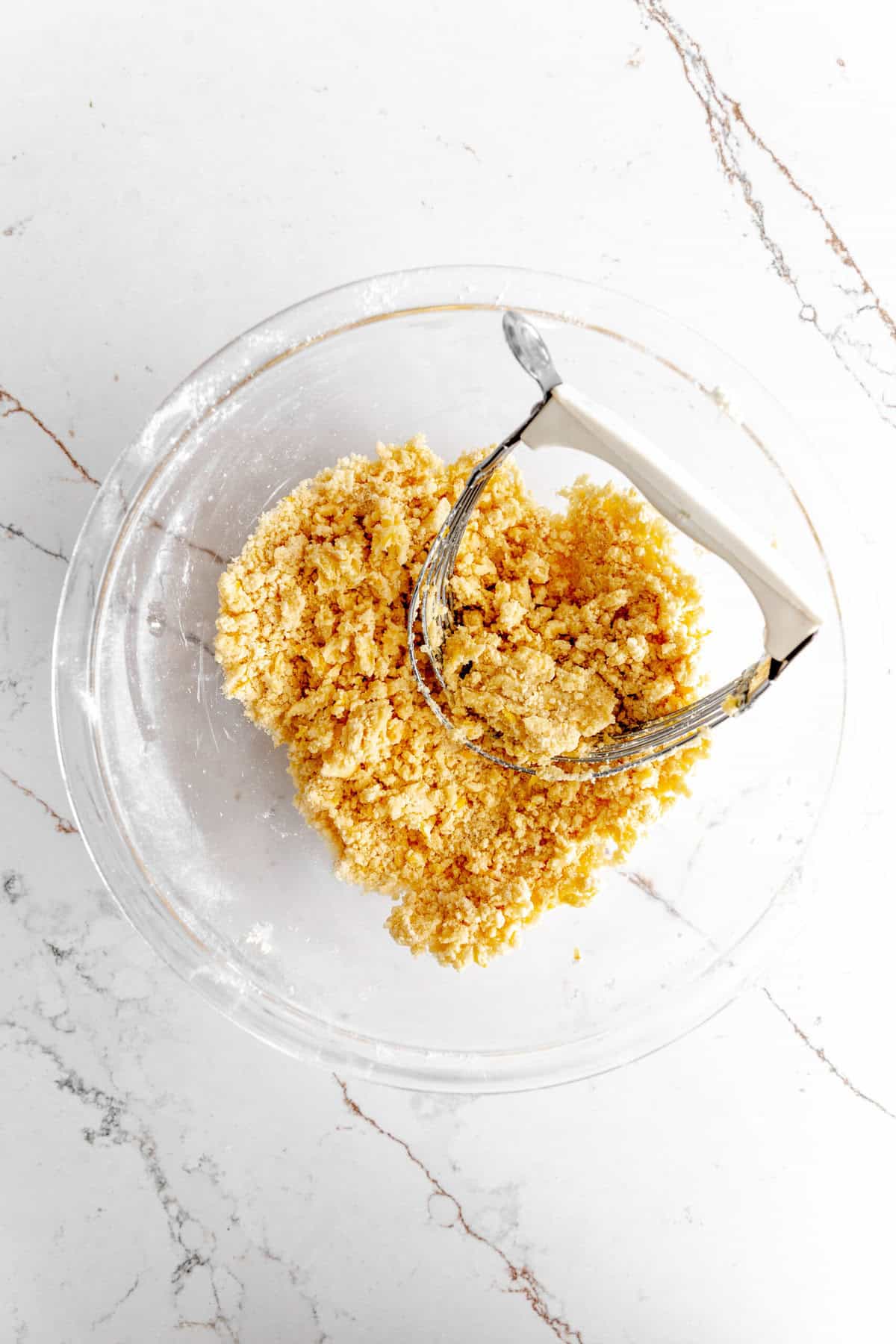 Glass bowl filled with crumbly butter, flour and a pastry cutter.