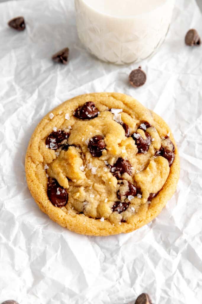 Chocolate chip cookie on a baking sheet with a glass of milk.