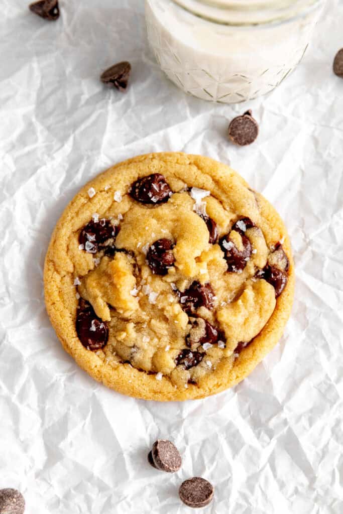 Chocolate chip cookie on a baking sheet with a glass of milk.