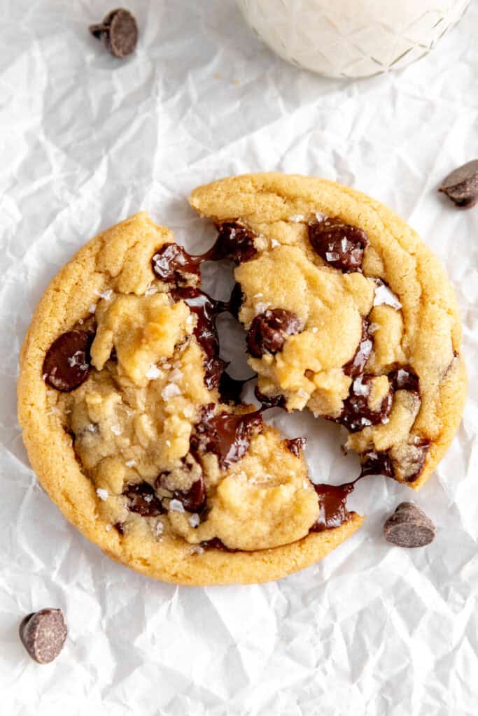 Gooey chocolate chip cookie halves being pulled apart and a glass of milk.