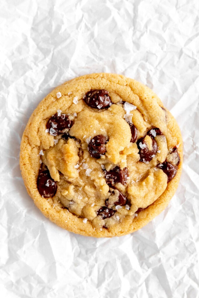 Chocolate chip cookie sprinkled with flaky sea salt on white parchment paper.