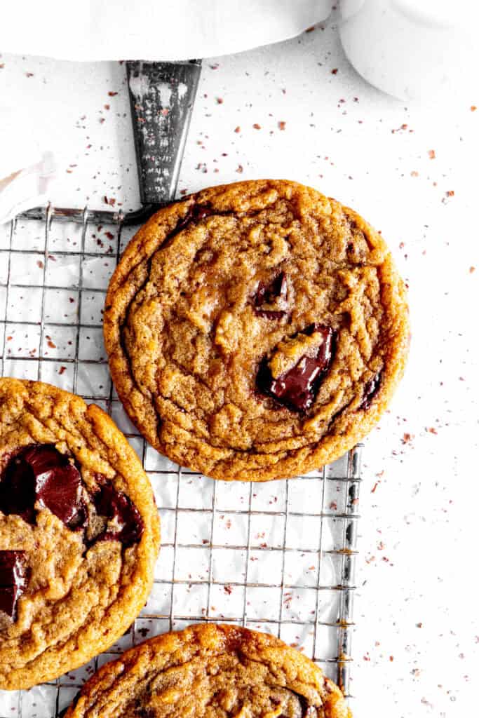 Toffee chocolate chip cookie on a wire rack, a linen napkin and a jug of milk.