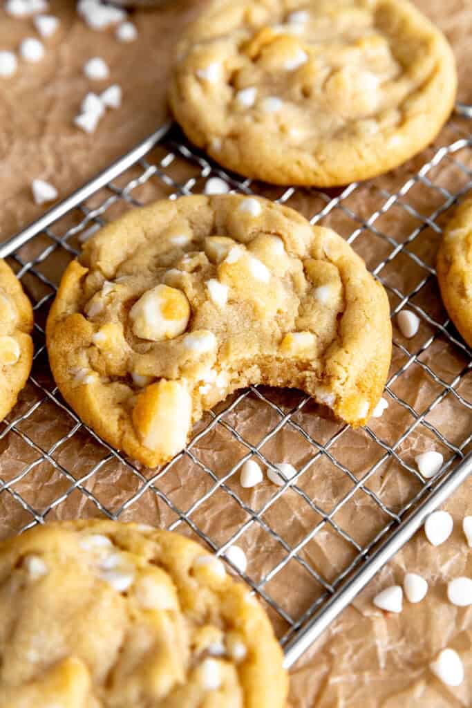 White chocolate macadamia cookie with a bite taken out of it on a wire rack.