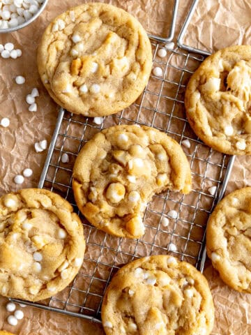 White chocolate macadamia cookies on a wire rack and brown parchment paper.