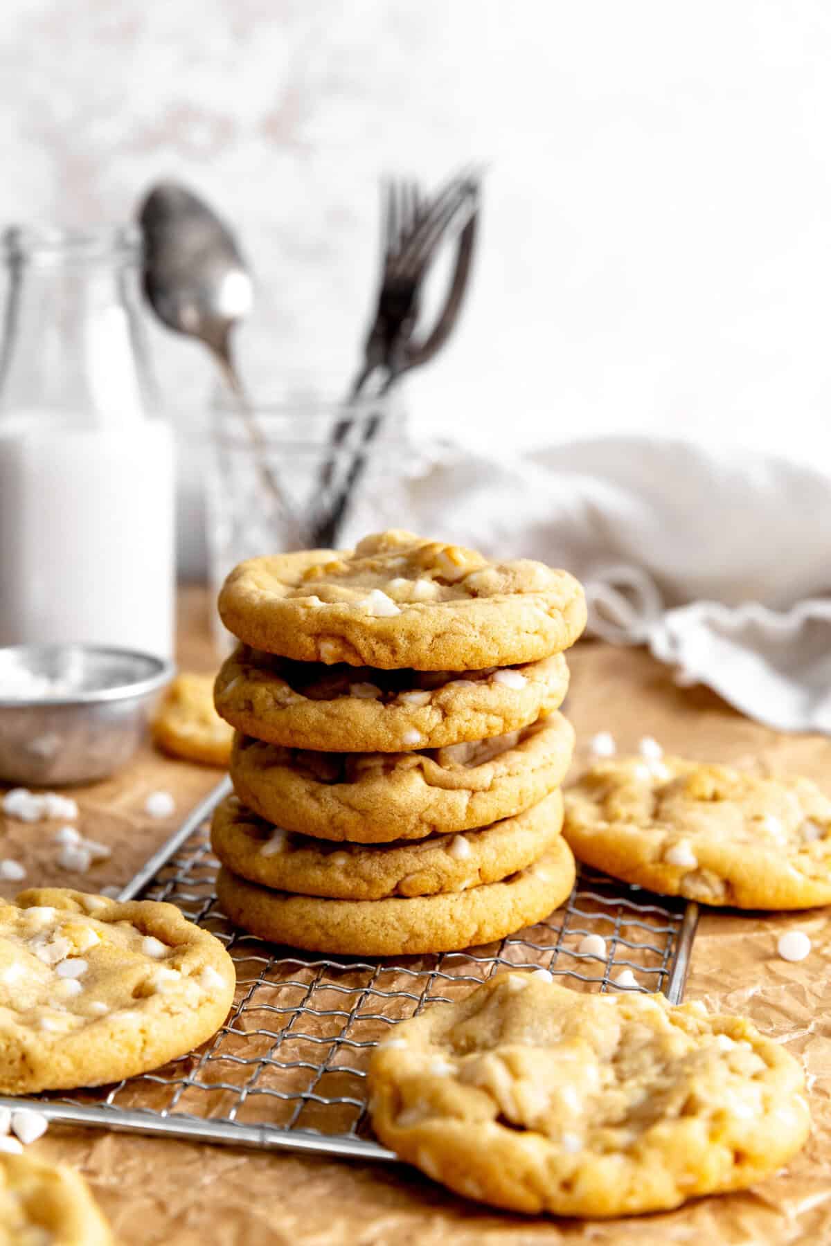 Stack of white chocolate macadamia cookies in front of a jug of milk and a cup of forks.