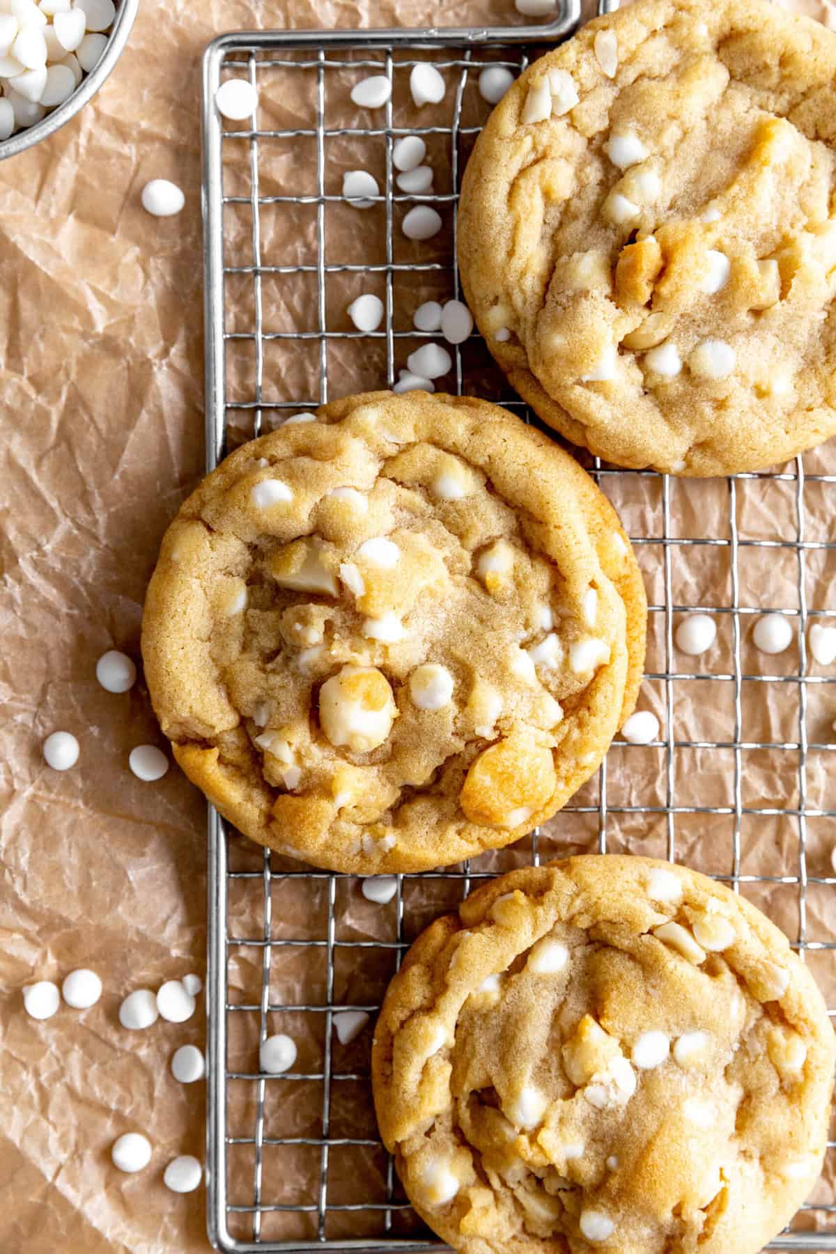 White chocolate macadamia cookies on a wire rack and a cup of white chocolate chips.