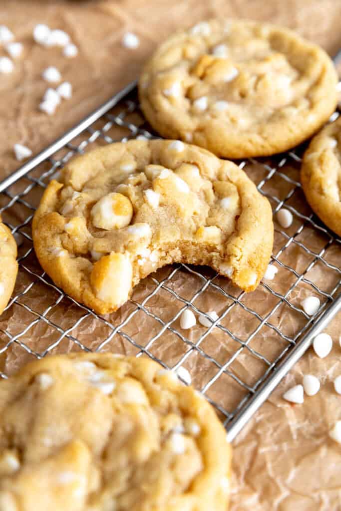 White chocolate macadamia cookie with a bite taken out of it on a wire rack.