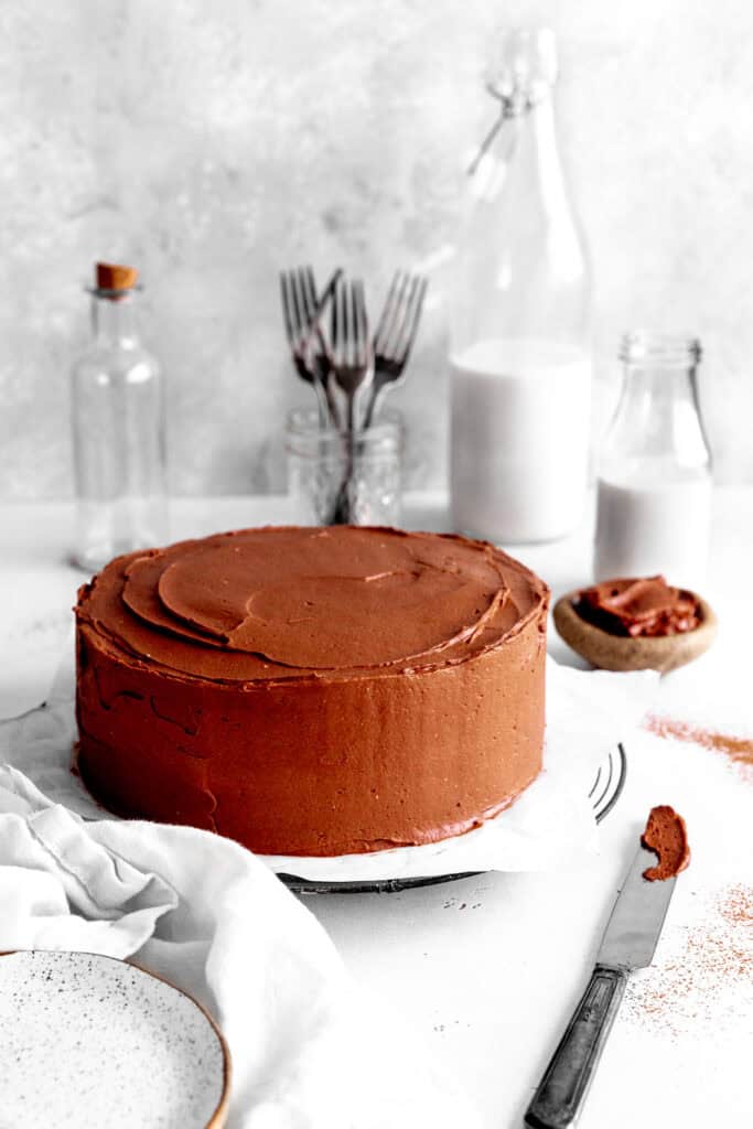 Chocolate cake, two jugs of milk, plates, forks and a knife covered in frosting.