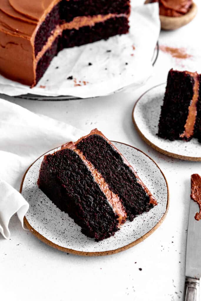 Chocolate cake on a wire cooling rack and two slices of chocolate cake on white plates.