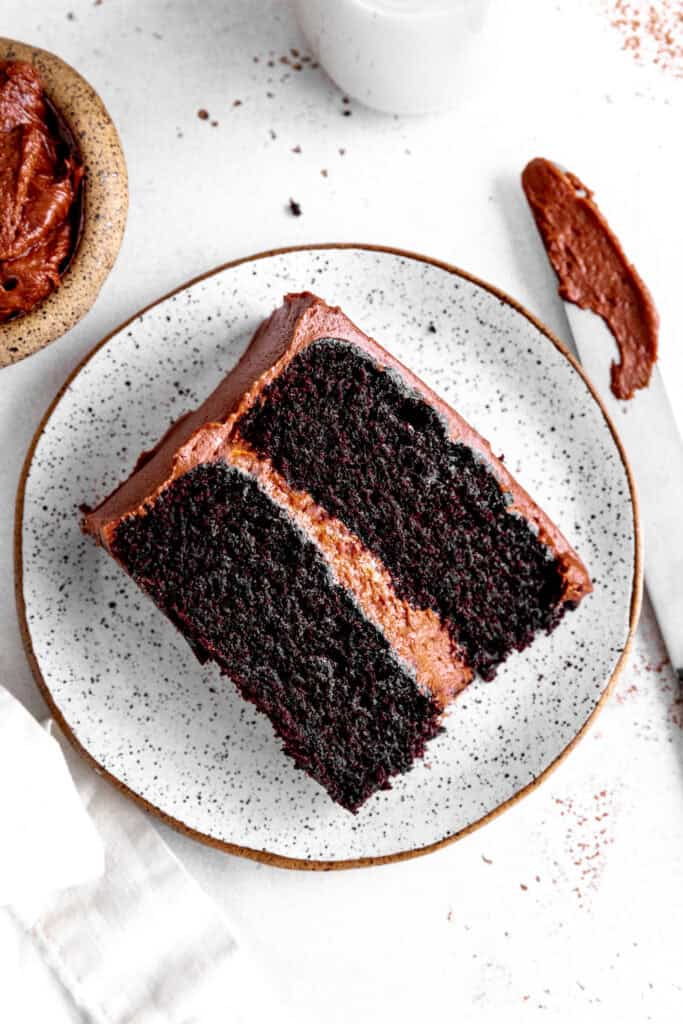 Slice of chocolate cake on a white plate, a jug of milk and a knife covered in frosting.