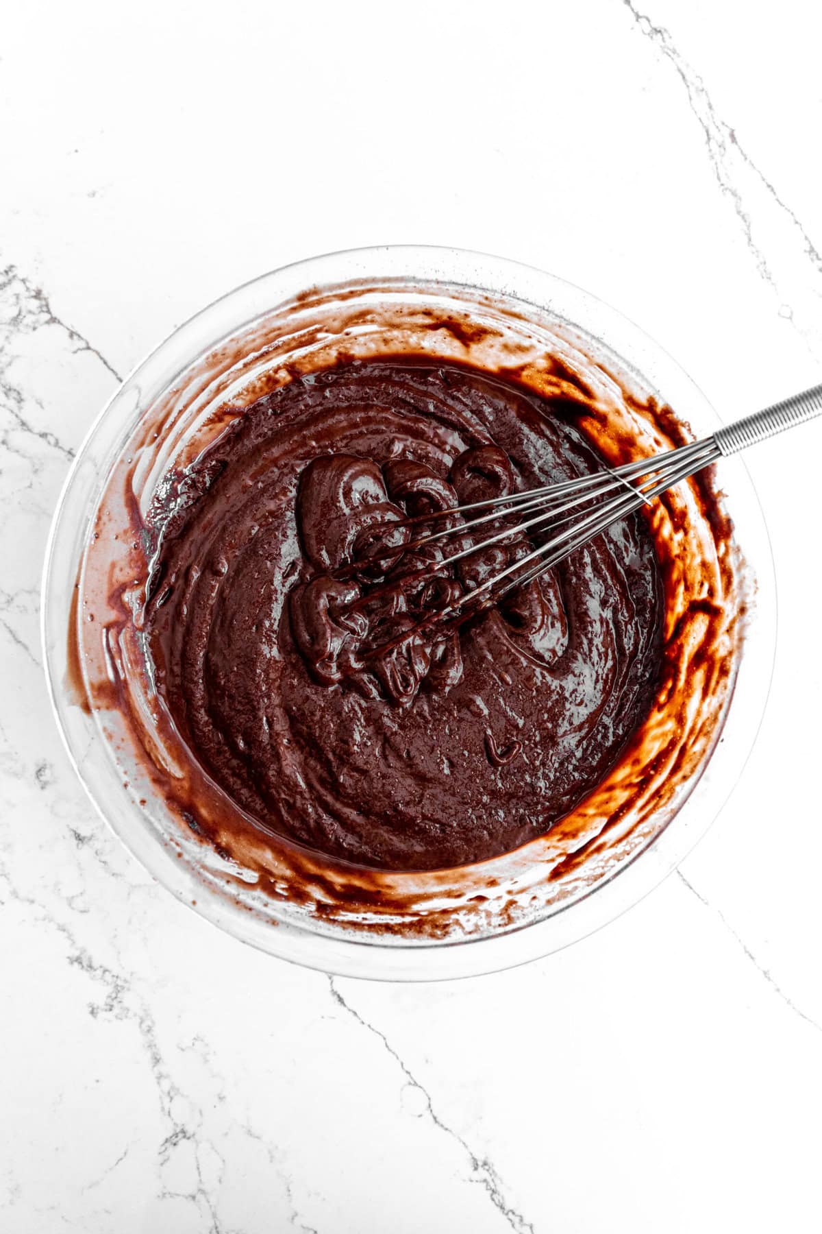 Glass bowl of chocolate cake batter and a wire whisk.