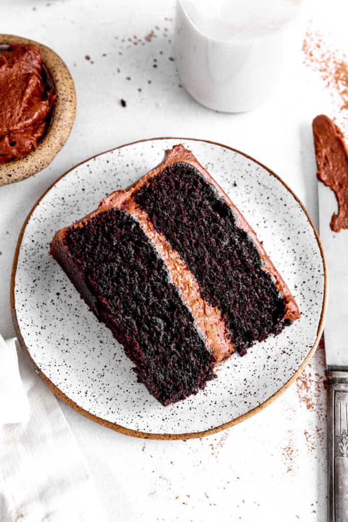 Slice of chocolate cake on a white plate, a jug of milk and a knife covered in frosting.