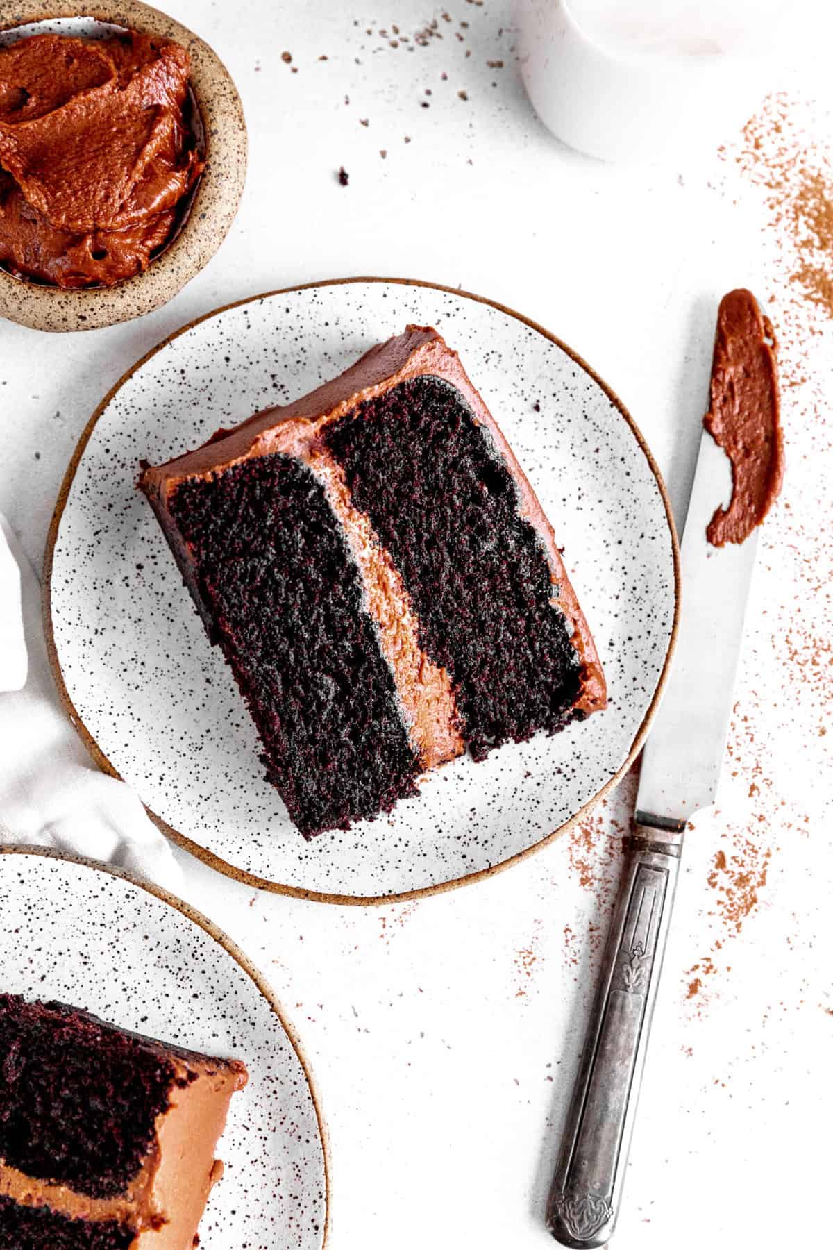 Two slices of chocolate cake on white plates, a jug of milk and a knife covered in frosting.