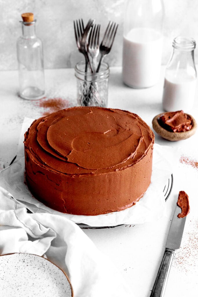 Chocolate cake, two jugs of milk, plates, forks and a knife covered in frosting.