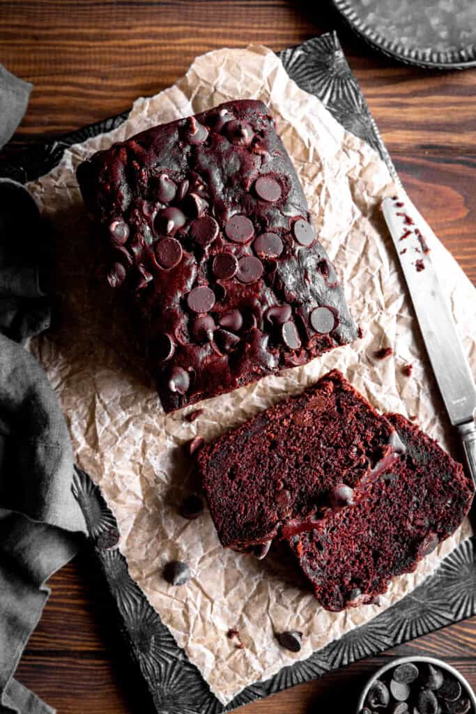 Sliced loaf of chocolate zucchini bread, a knife and a cup of chocolate chips.