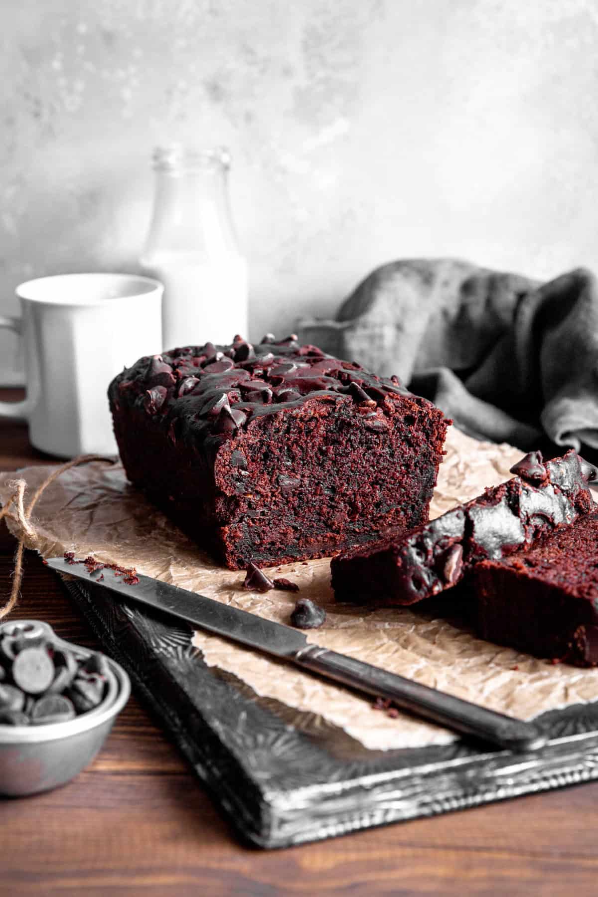 Loaf of chocolate zucchini bread in front of a mug and a jug of milk.