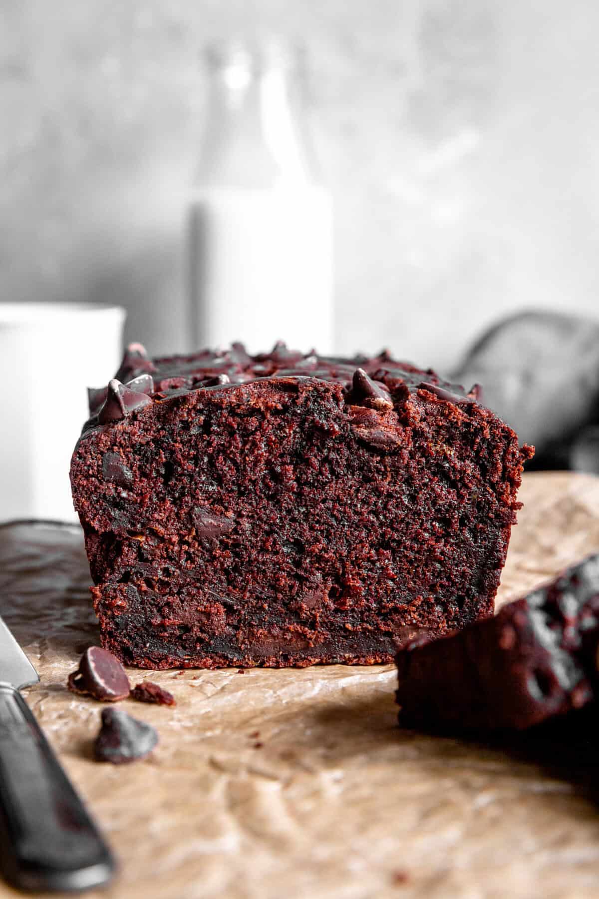 Loaf of chocolate zucchini bread in front of a jug of milk.