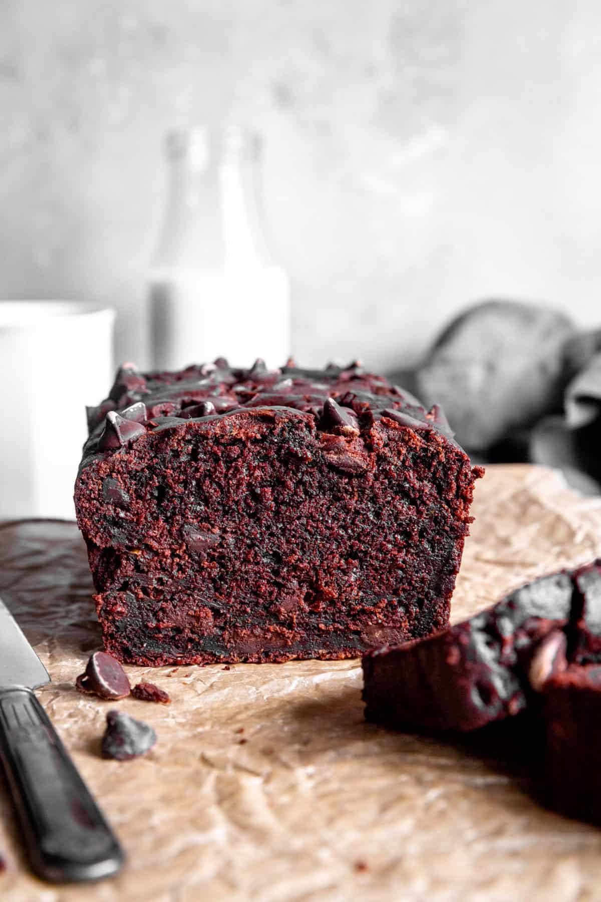 Loaf of chocolate zucchini bread and a knife in front of a jug of milk.