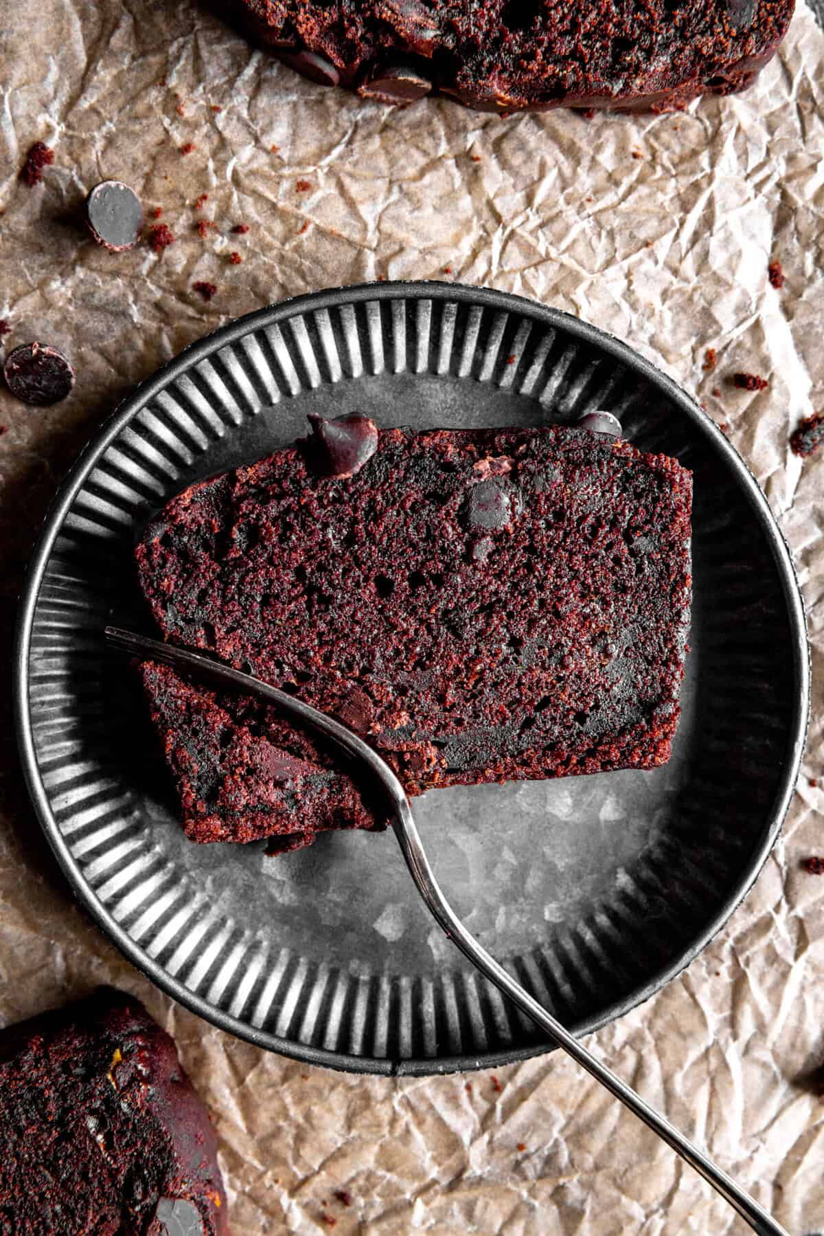 Fork cutting into a slice of chocolate zucchini bread on a metal plate.