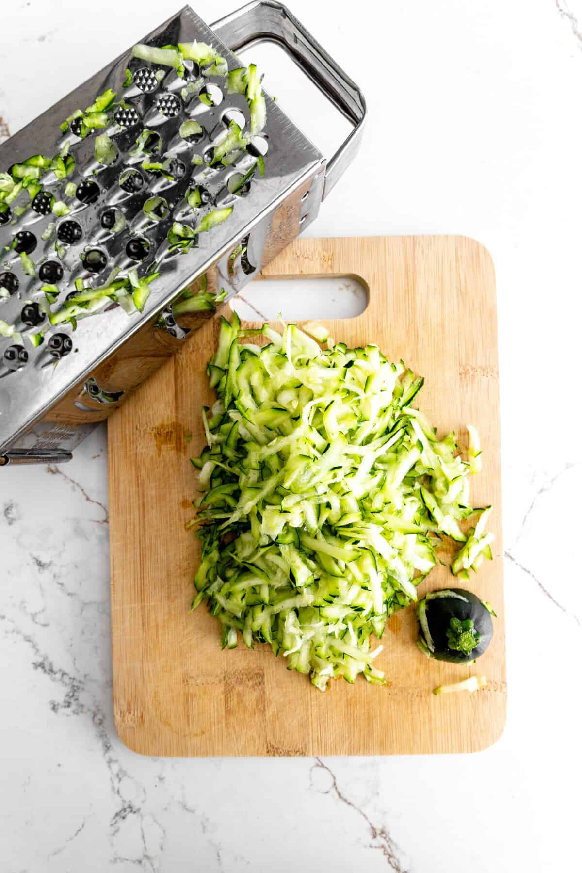 Shredded zucchini on a cutting board with a box grater.