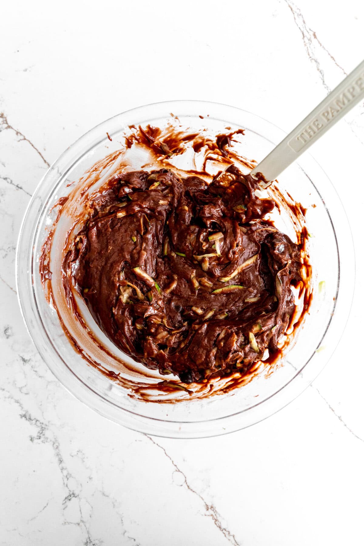 Chocolate zucchini bread batter in a glass bowl with a rubber spatula.