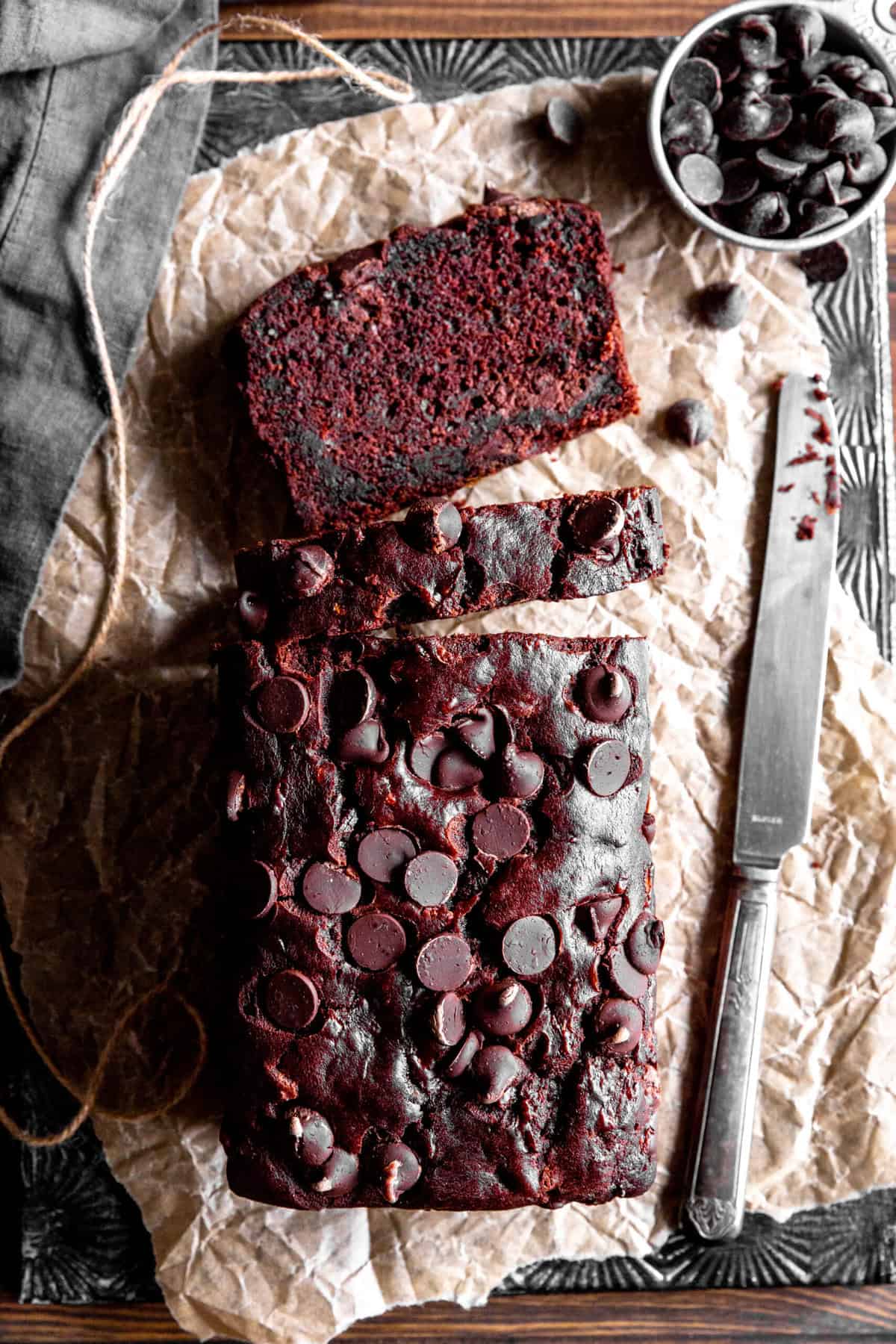 Sliced loaf of chocolate zucchini bread, a knife and a cup of chocolate chips.