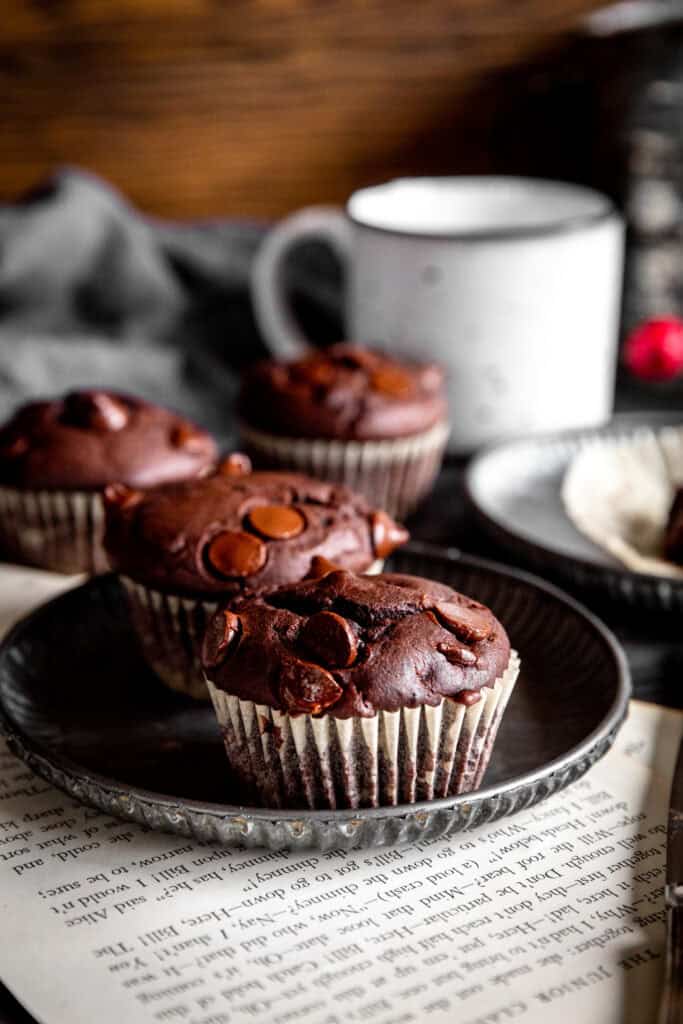 Two chocolate muffins on a metal plate, a gray linen napkin and a white mug.