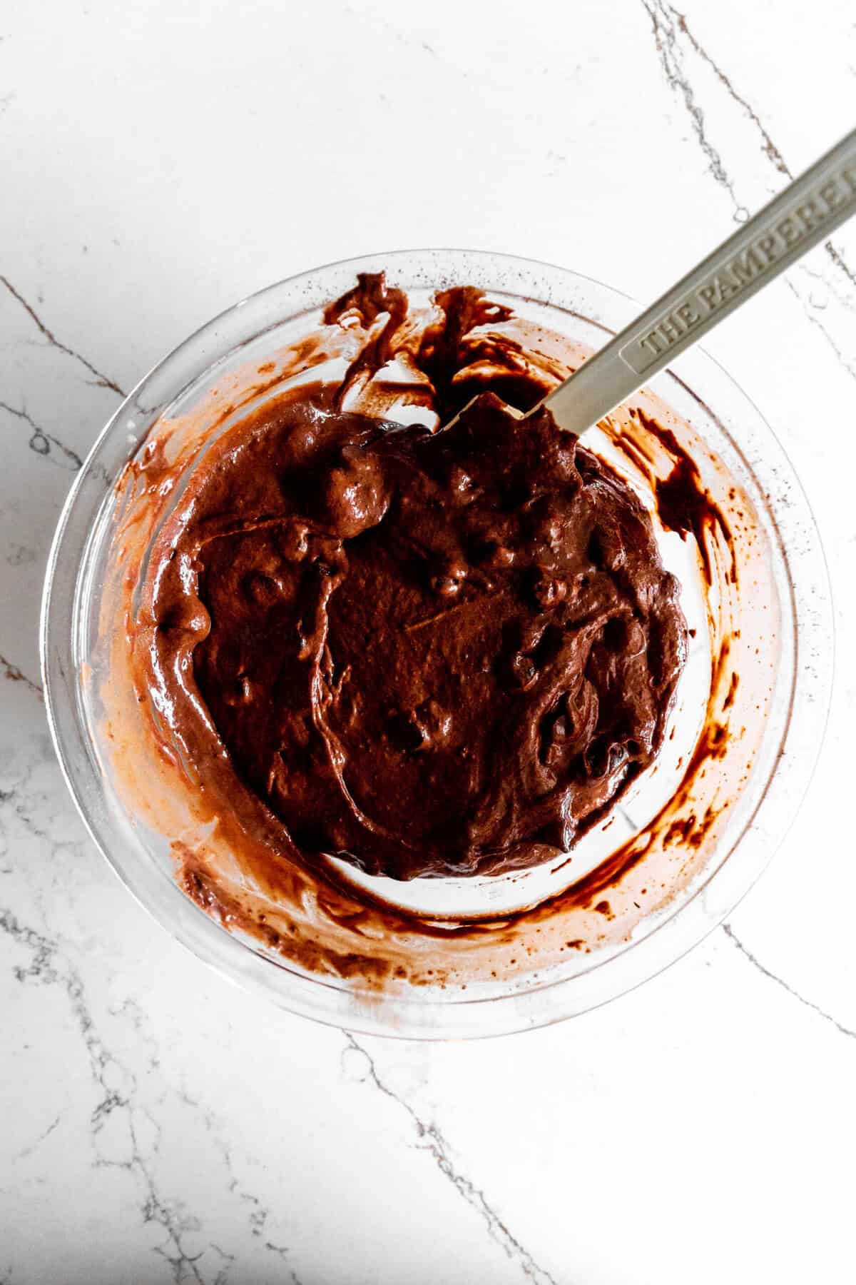 Glass bowl filled with chocolate muffin batter and a rubber spatula.