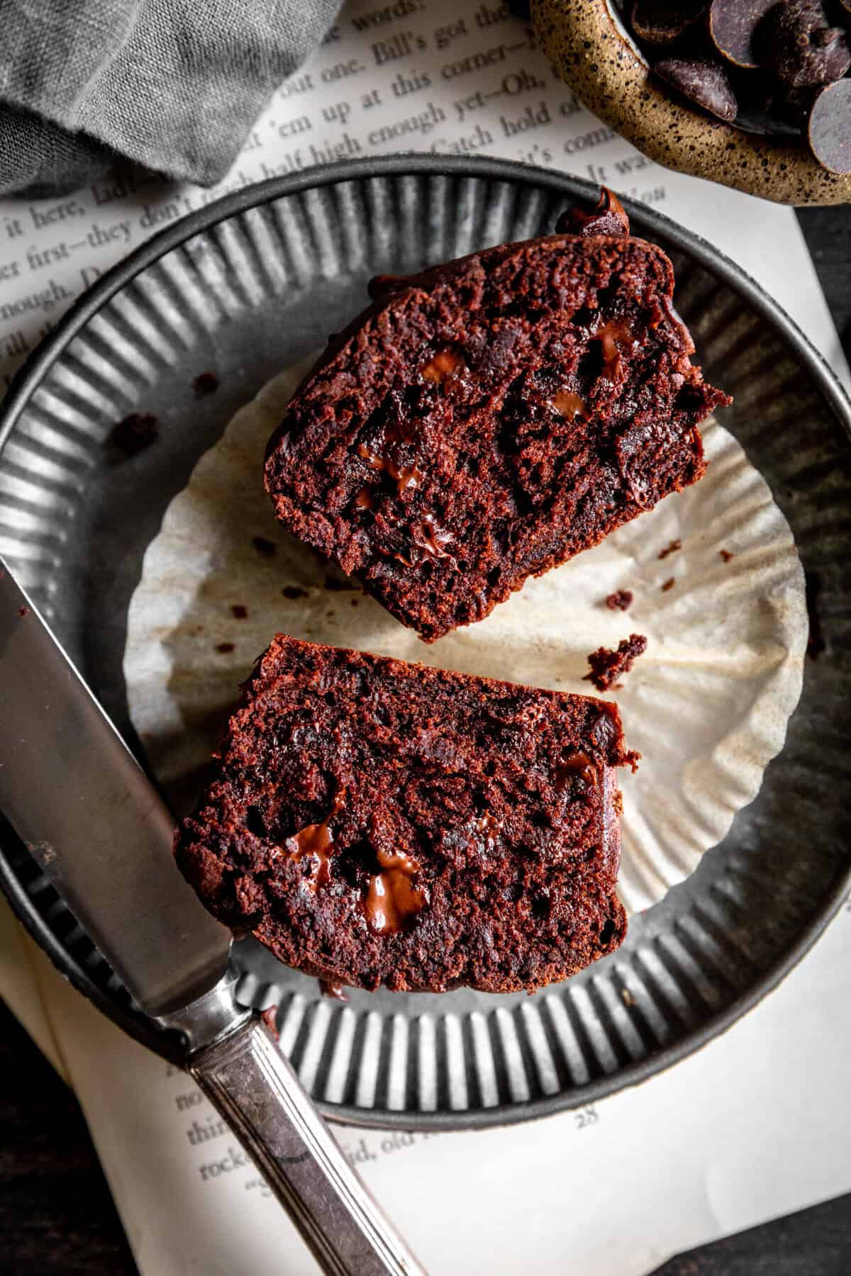 Two chocolate muffin halves on a metal plate with a knife.