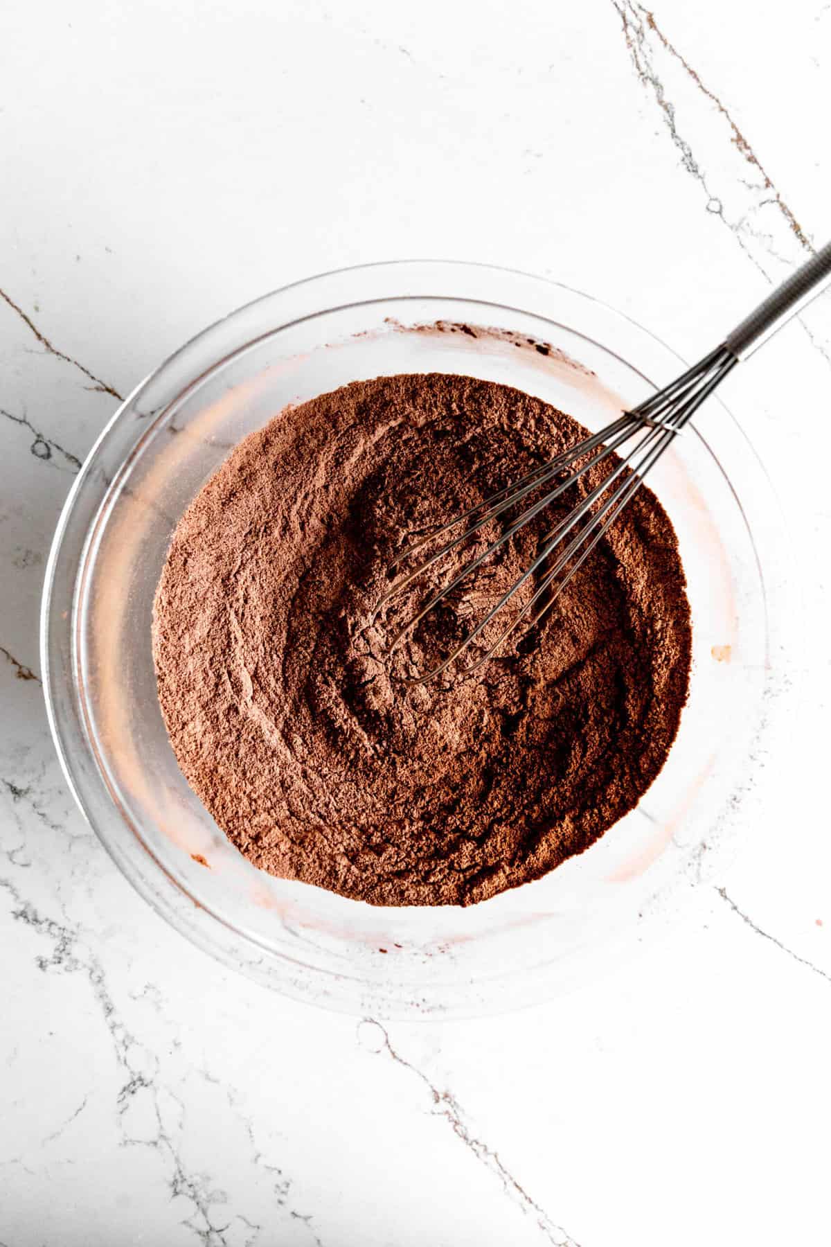 Glass bowl filled with flour, cocoa powder and a wire whisk.