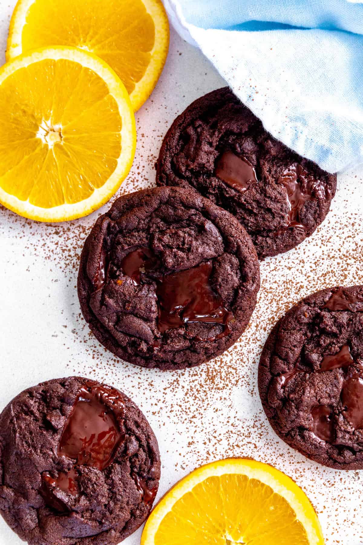 Orange chocolate cookies layered on a white surface with orange slices.