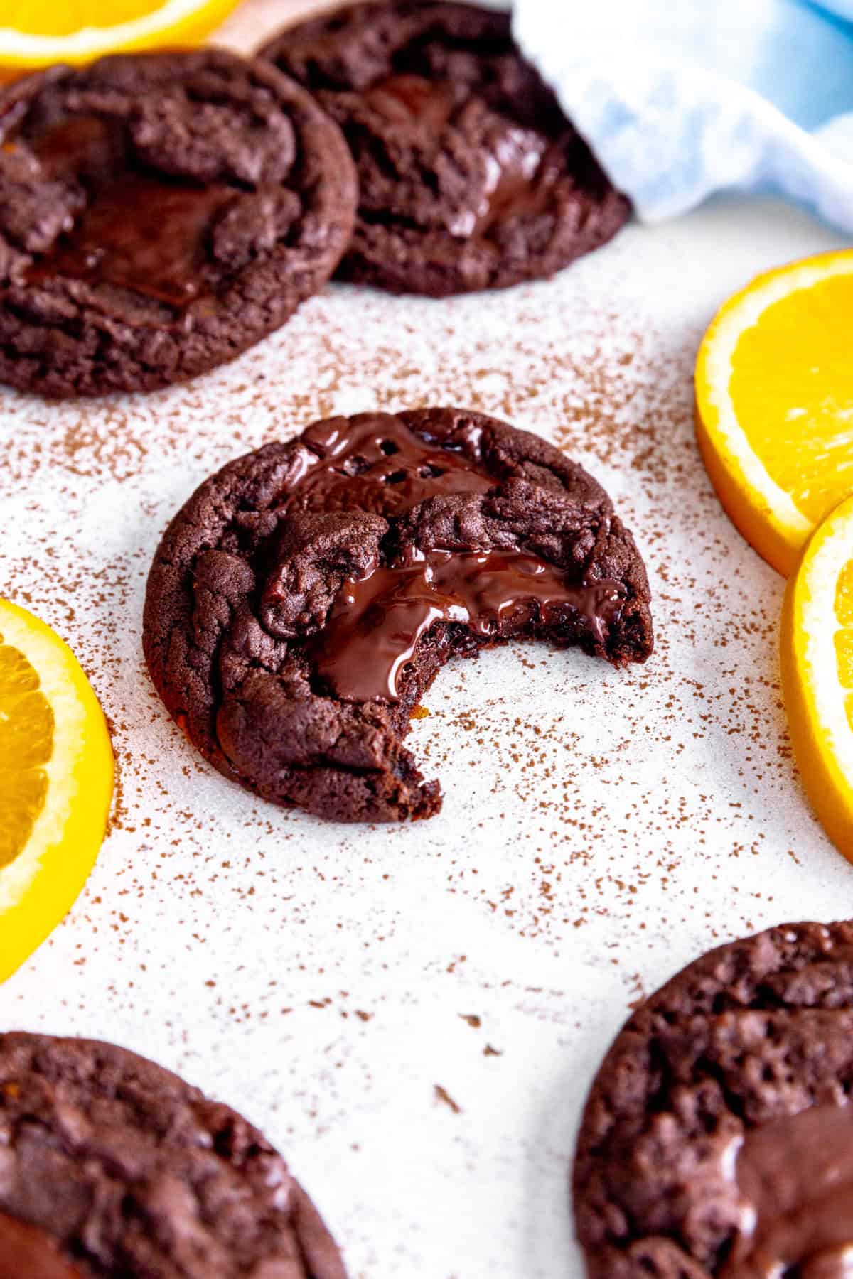 Orange chocolate cookie with a bite taken out of it surrounded by more cookies and orange slices.