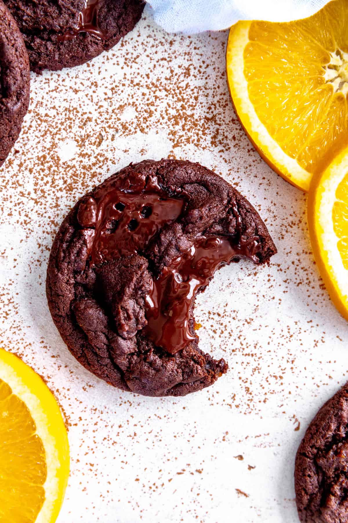 Orange chocolate cookie with a bite taken out of it and fresh orange slices.