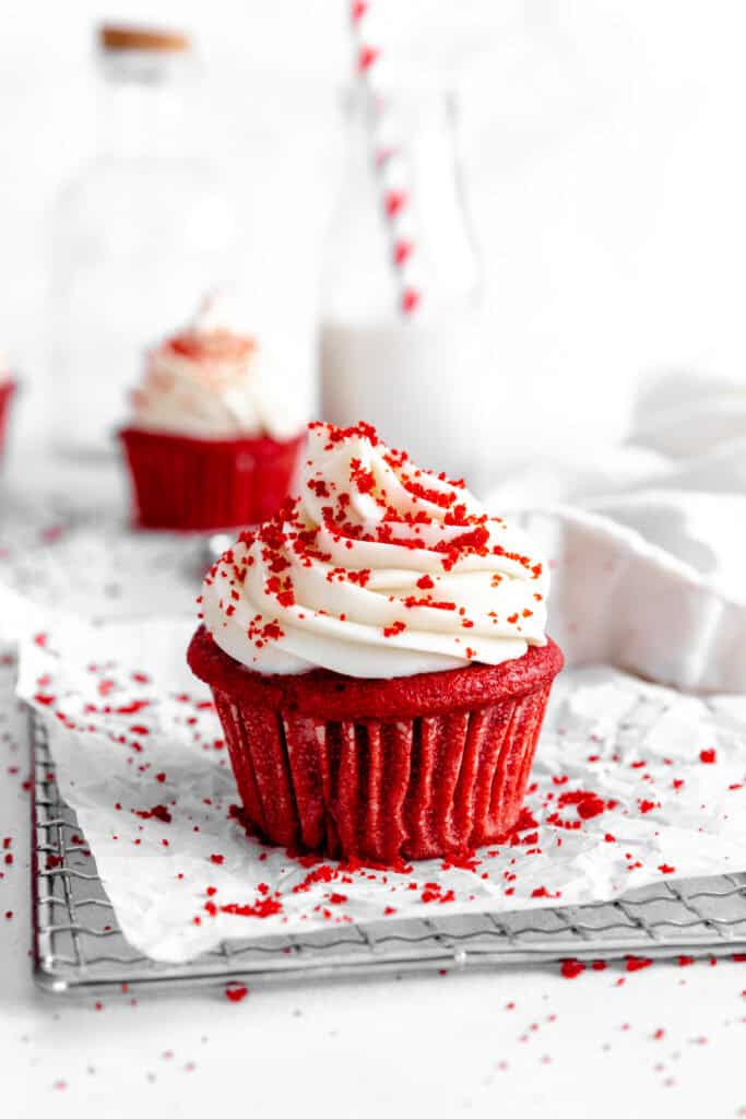 Red velvet cupcake on a wire cooling rack in front of a jug of milk.