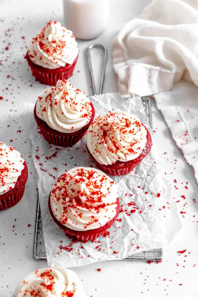 Red velvet cupcakes on a wire cooling rack, a white linen napkin and a jug of milk.