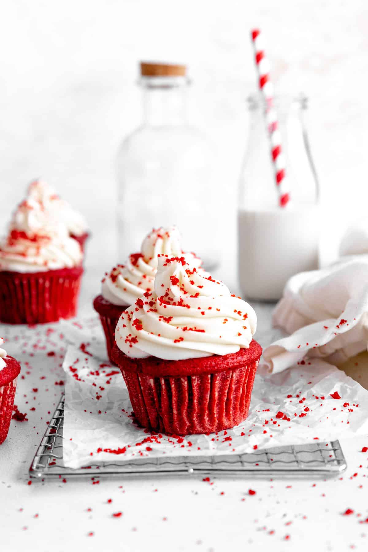 Red velvet cupcakes on a wire cooling rack, a jug of milk and a white linen.