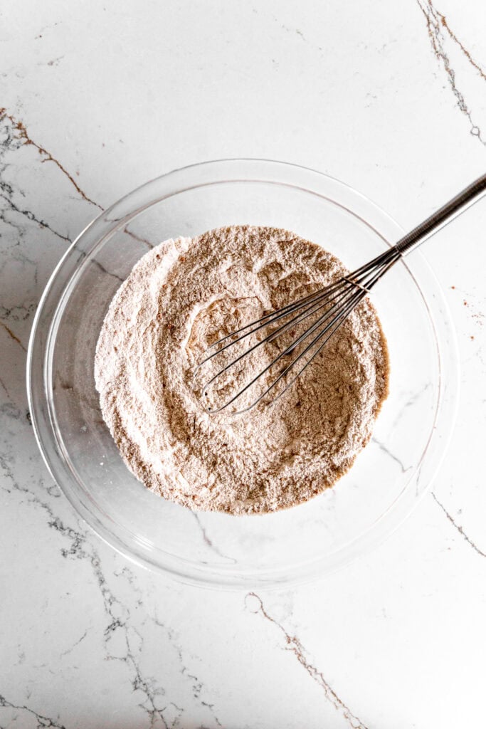 Glass bowl of dry cake ingredients and a wire whisk.