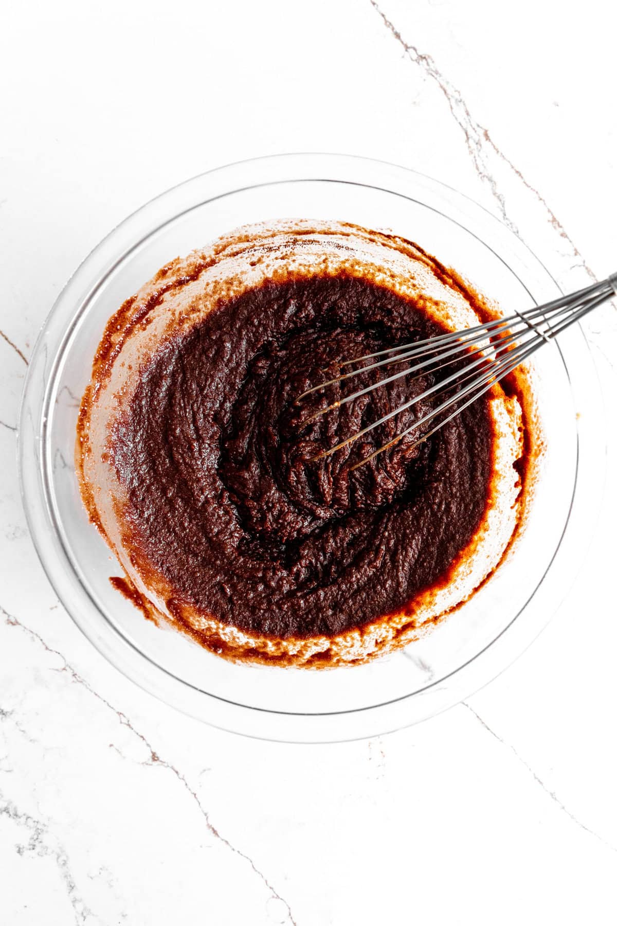 Melted chocolate and sugar in a glass bowl with a wire whisk.