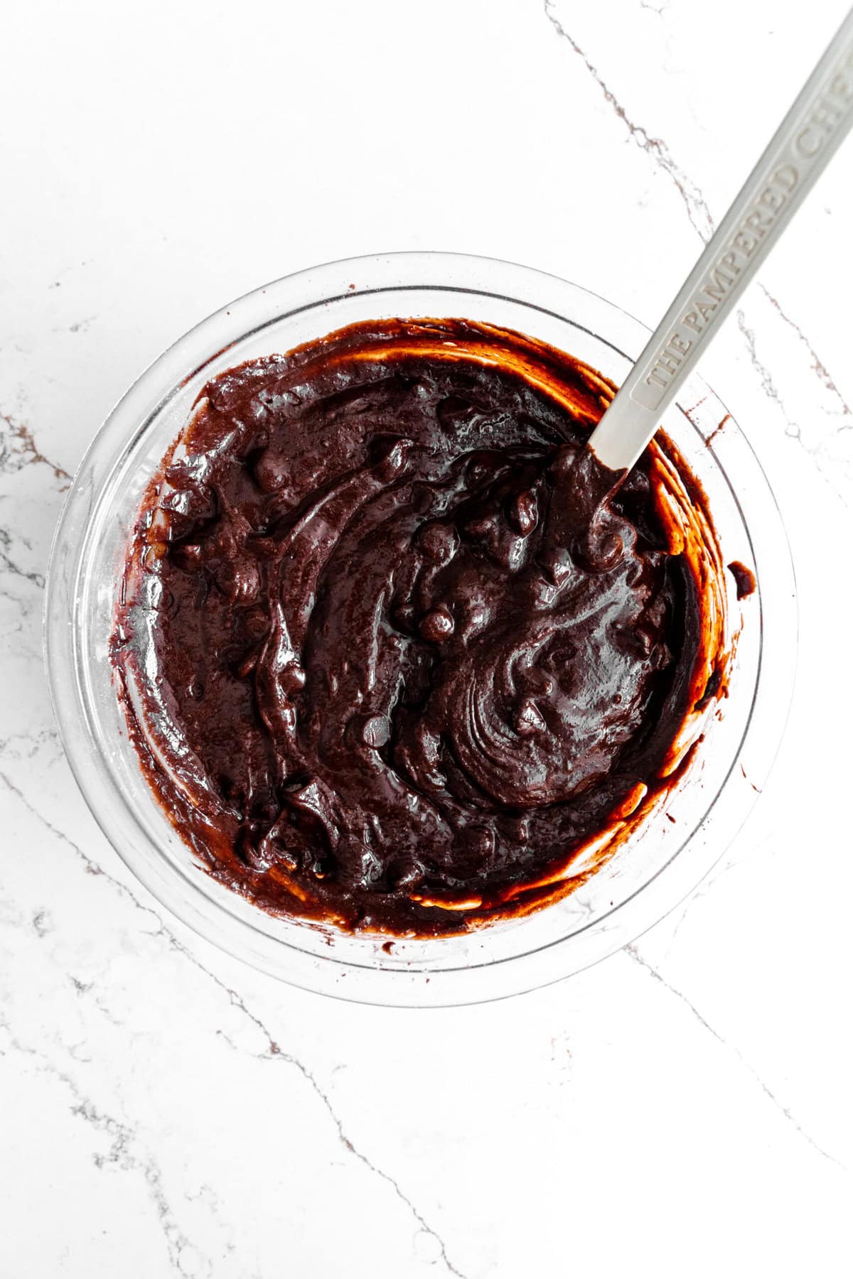 Brownie batter in a glass bowl with a rubber spatula.