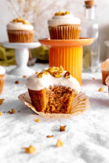 Carrot cake cupcake with a bite taken out of it surrounded by more cupcakes.