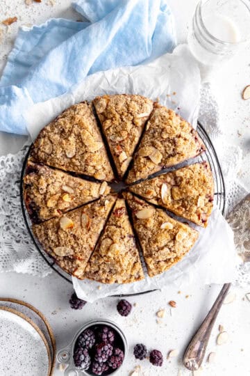 Blackberry almond scones on a wire cooling rack, a glass of milk and a cup of blackberries.