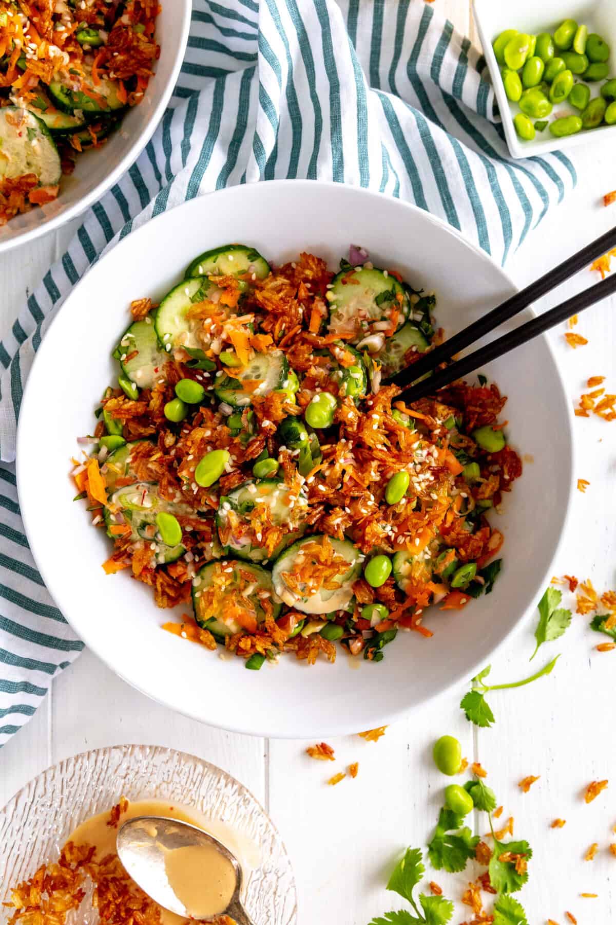 Chopsticks digging into a bowl of cucumber salad topped with crispy rice and a bowl of edamame.