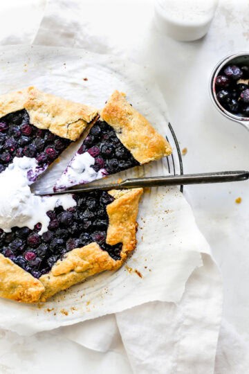 Knife cutting into a blueberry galette with a slice pulled out and a cup of milk.