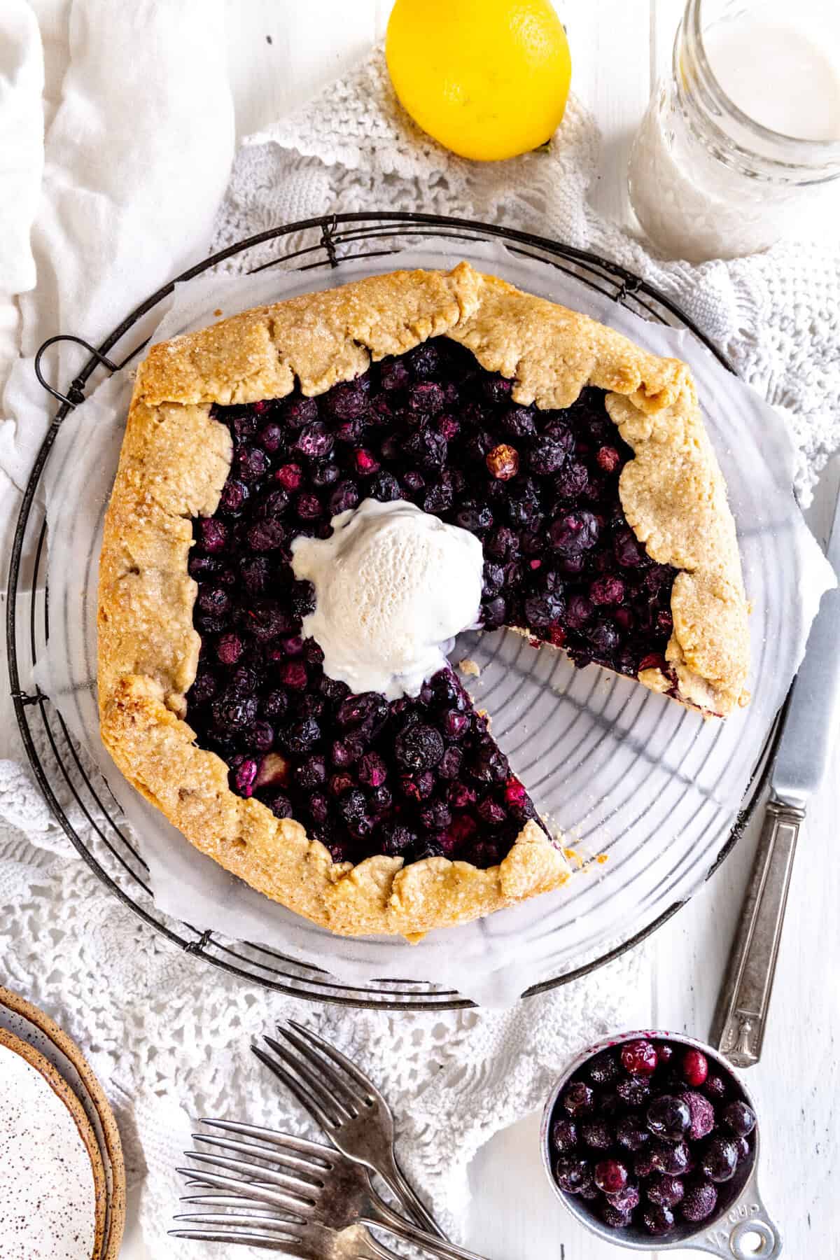 Blueberry galette missing a slice, a cup of milk, a lemon and a cup of blueberries.